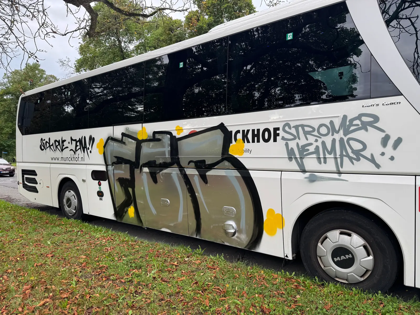 Graffiti mit schwarzen Konturen, grauen Flächen und gelben Punkten auf weißem Reisebus vor der Reinigung